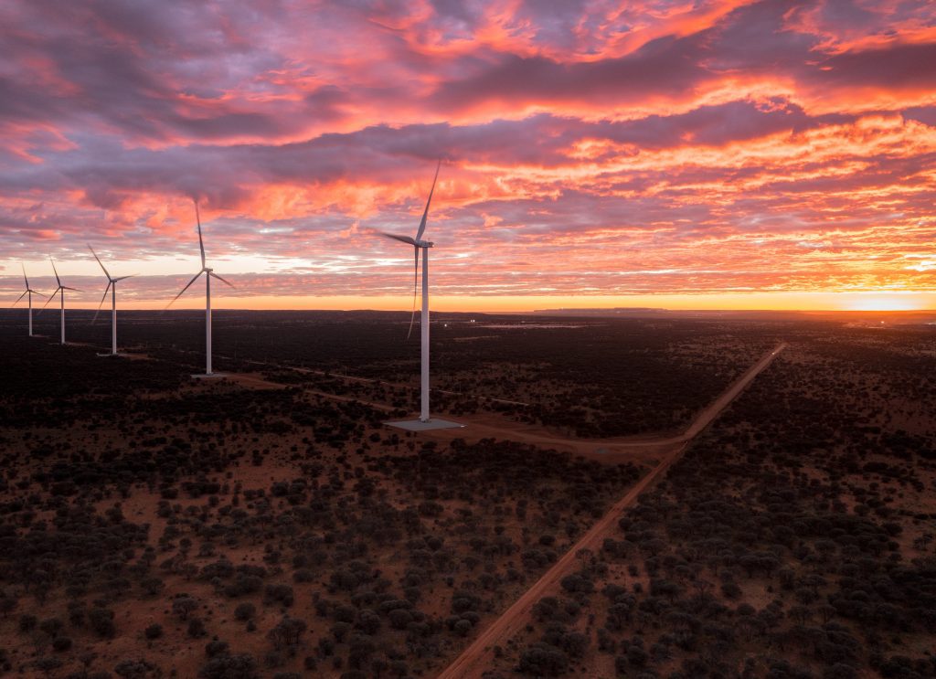 Wind turbines towering over the Western Australian desert against a brilliant orange, purple and yellow sunset